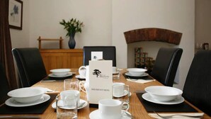 A dining table set for breakfast with a menu stand, chairs, and a vase of flowers.