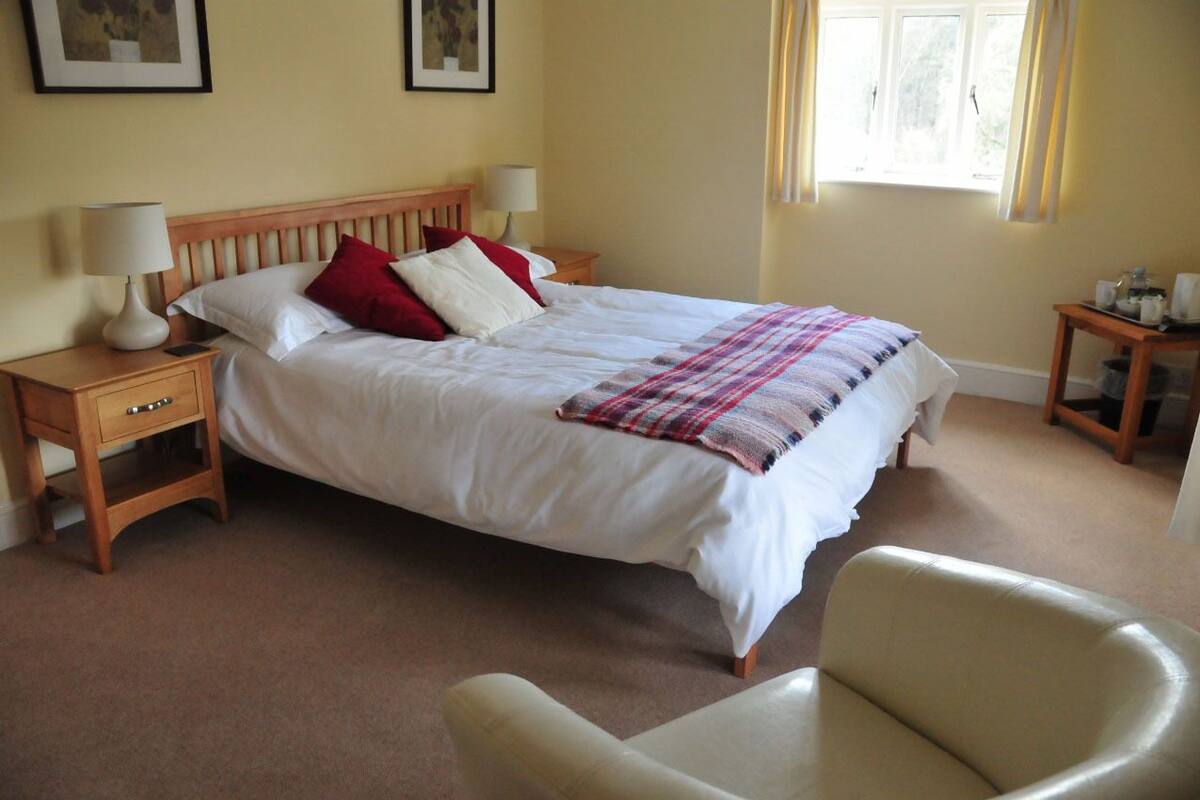 A neatly arranged bedroom with a large bed, bedside tables, a chair, and a window with curtains.