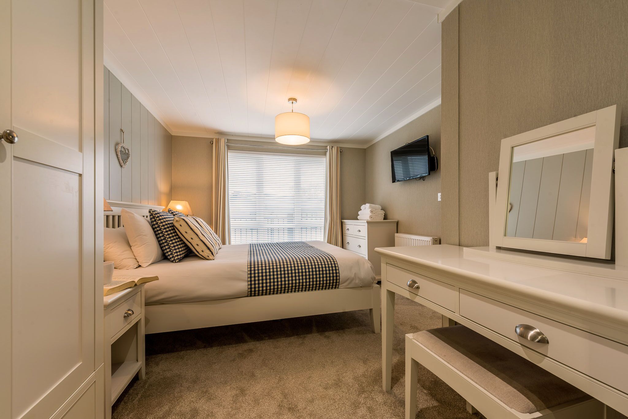 A bedroom with a bed, bedside table, lamp, dresser, and a television on the wall.