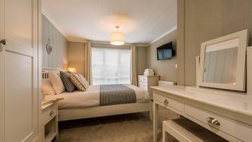 A bedroom with a bed, bedside table, lamp, dresser, and a television on the wall.