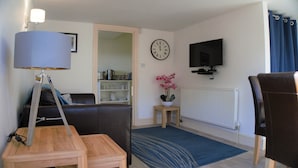 Una sala de estar con un sofá, una mesa de centro, una lámpara, un reloj, un televisor y un radiador.