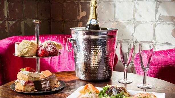 A dessert trolley with cakes and strawberries, a champagne bottle in a metal bucket, and a plate of appetizers on a wooden table. - The Lounge Hotel and Bar (Penrith)