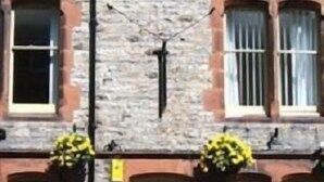 A two-story building with a stone facade, a wooden door, and windows with shutters. There are potted plants on the ground floor. - The Lounge Hotel and Bar (Penrith)