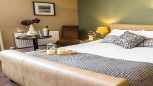 A neatly arranged bedroom with a large bed, bedside lamps, a small table with a vase and a lamp, and a chair. - The Lounge Hotel and Bar (Penrith)