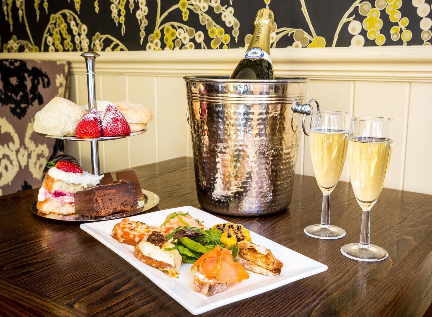 A table with a variety of food items, a champagne bottle, and two glasses of champagne.