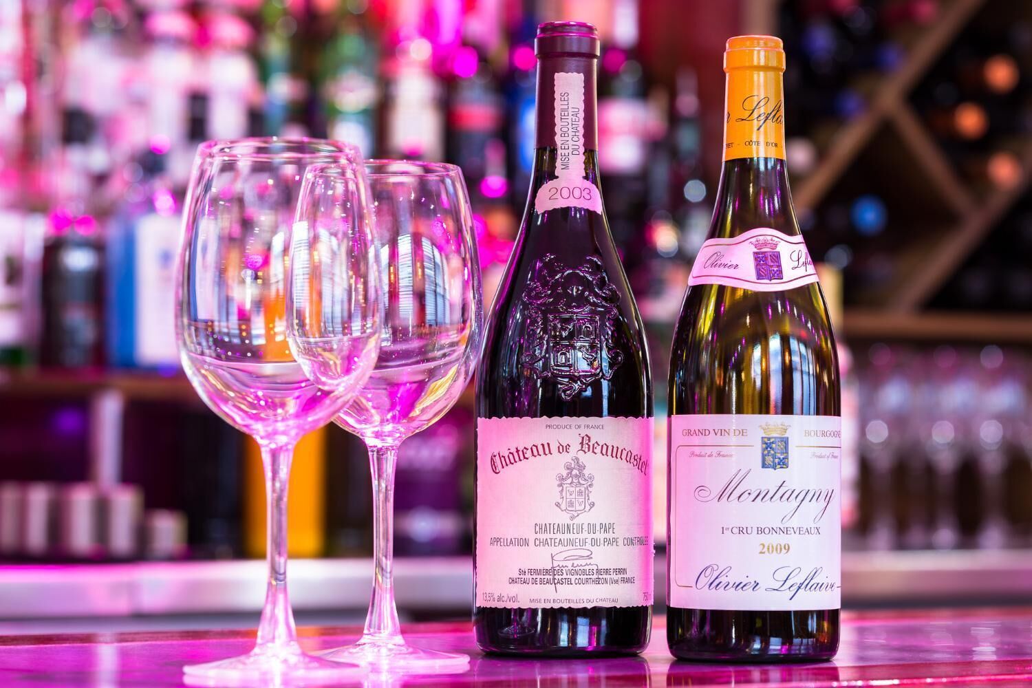 Two wine bottles and two empty wine glasses on a bar counter.