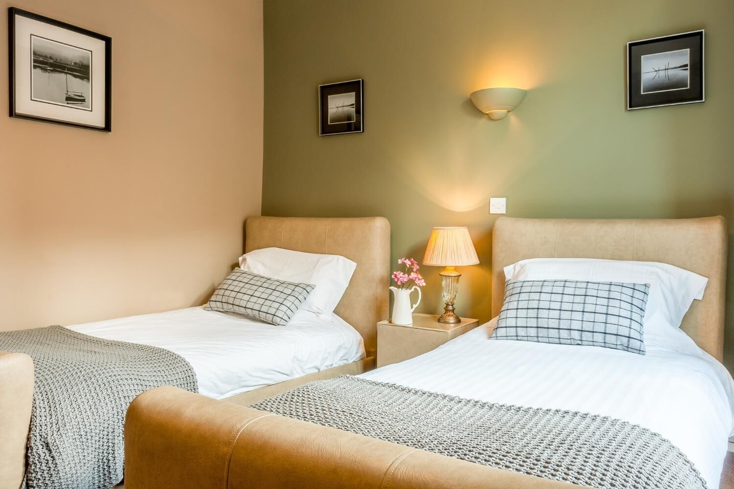 A hotel room with two beds, a nightstand with a lamp, and framed pictures on the walls.