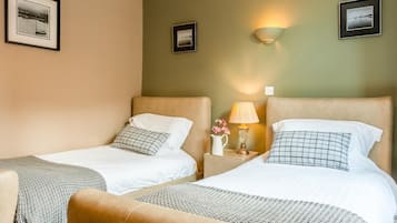 A hotel room with two beds, a nightstand with a lamp, and framed pictures on the walls.