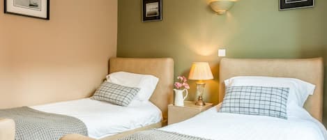 A hotel room with two beds, a nightstand with a lamp, and framed pictures on the walls.