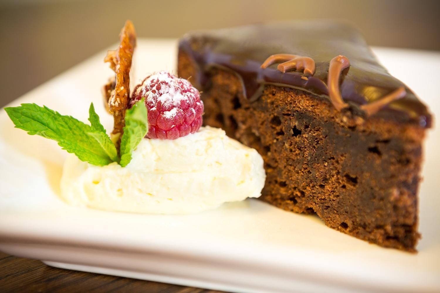 Una porción de pastel de chocolate con frambuesa encima, acompañada de una bola de helado de vainilla y una hoja de menta como adorno.
