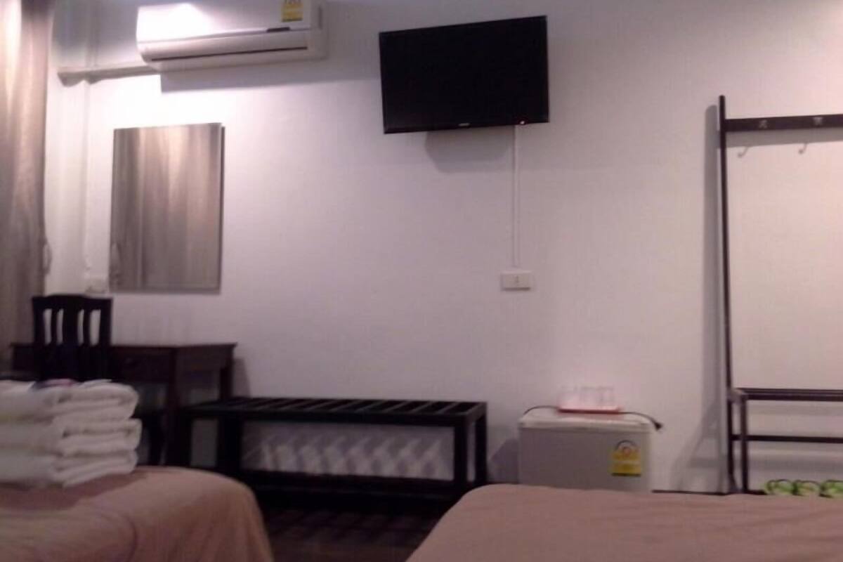 Een hotelkamer met twee bedden, een aan de muur bevestigde televisie, een airconditioner, een klein tafeltje met een stoel, en een radiator.