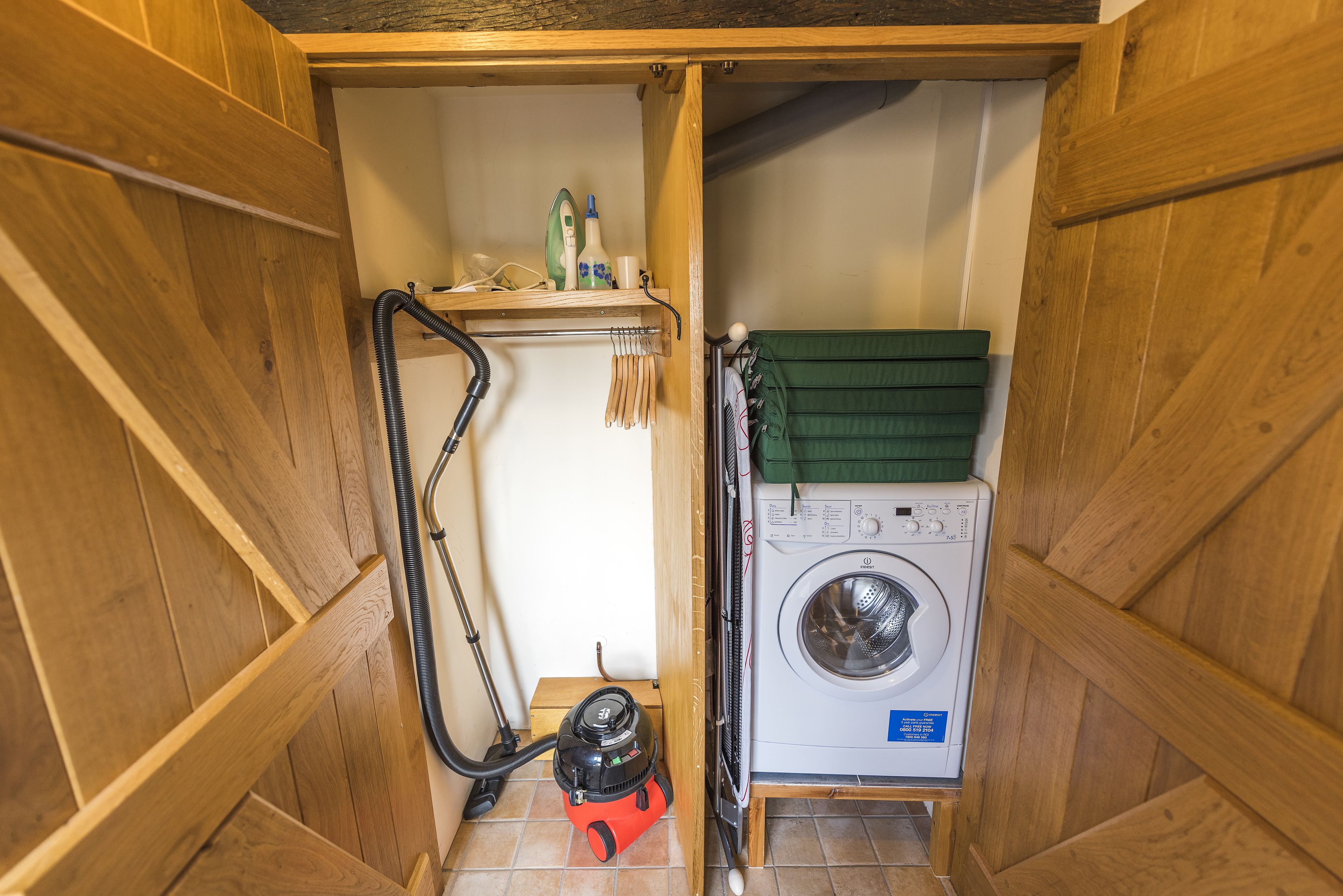 A compact laundry room with a washing machine, a vacuum cleaner, and a shelf with cleaning supplies.
