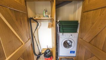 A compact laundry room with a washing machine, a vacuum cleaner, and a shelf with cleaning supplies.