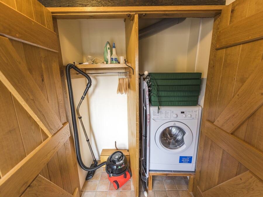 A compact laundry room with a washing machine, a vacuum cleaner, and a shelf with cleaning supplies.