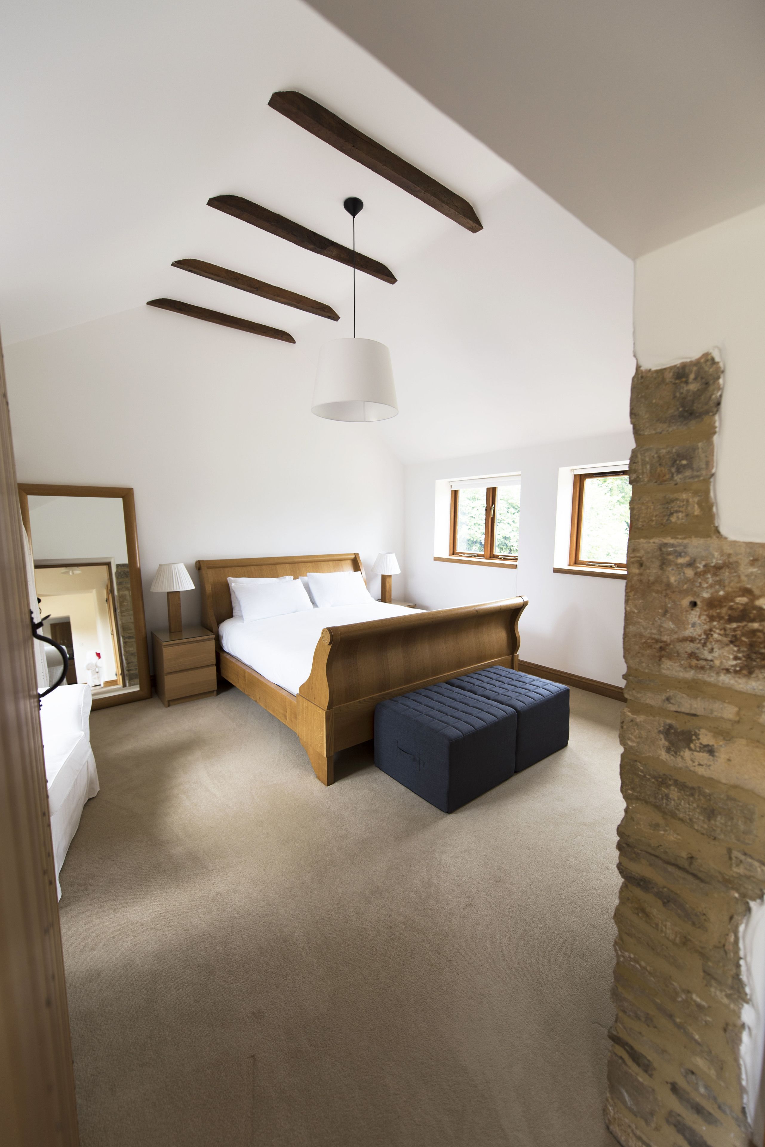 Une chambre avec un lit en bois, une table de chevet, une lampe, un banc et un mur en pierre.