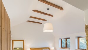 Un dormitorio con una cama de madera, mesitas de noche, una lámpara colgante y ventanas.
