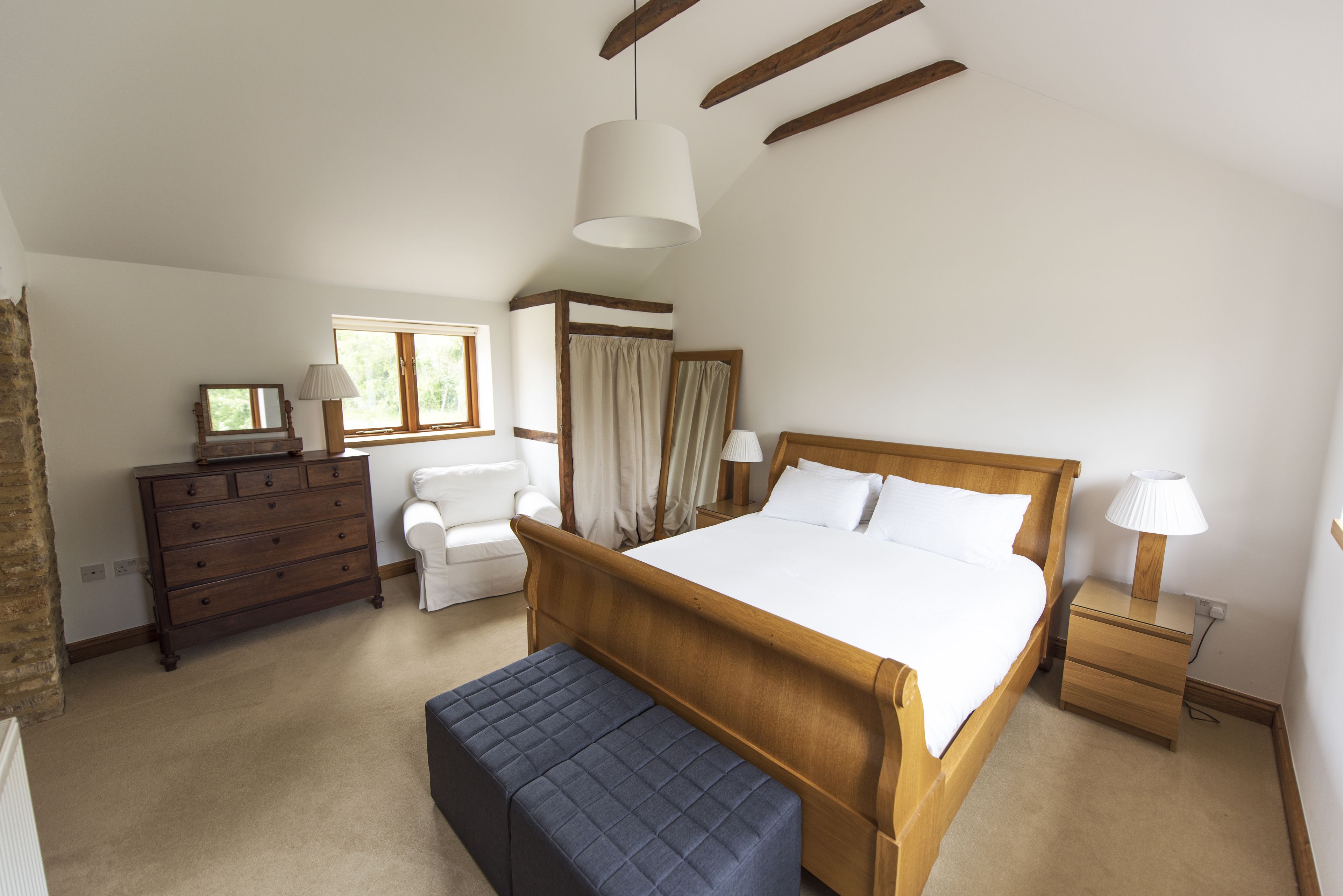 A bedroom with a wooden bed, a dresser, a bench, a nightstand, and a window with curtains.