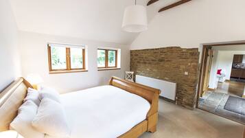 Een slaapkamer met een houten bed, twee ramen, een stenen muur en uitzicht op een andere kamer.