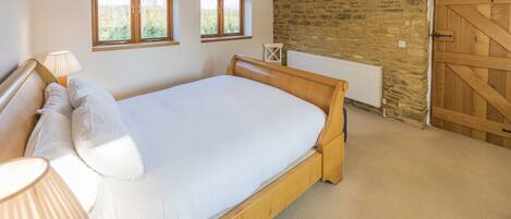 A bedroom with a wooden bed, two windows, a stone wall, a radiator, and a wooden door.