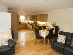 Een moderne keuken met houten kastjes, een eettafel met stoelen, en een zithoek met een bank en salontafel.