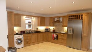 Una cocina moderna con armarios de madera, un refrigerador de acero inoxidable, horno empotrado, microondas y lavadora.