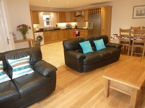 A living room with two black leather sofas, a wooden coffee table, and a kitchen in the background.