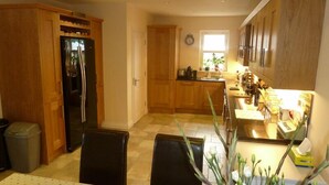 Una cocina con armarios de madera, un refrigerador, una mesa de comedor con sillas y una ventana con luz natural.