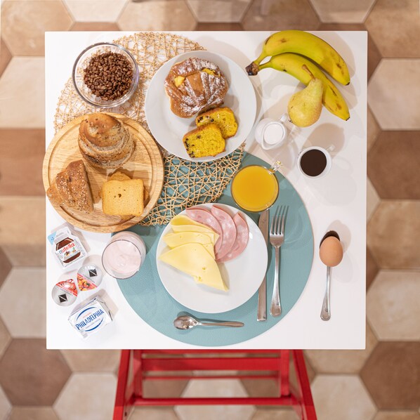 Une table de petit-déjeuner avec divers aliments, notamment du pain, des viennoiseries, du fromage, du jambon et des œufs.