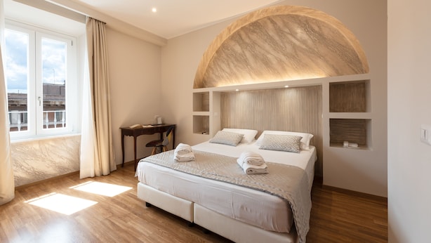 A modern bedroom with a large bed, a curved wall feature, and a desk with a chair. - Top Floor Colosseo (Rome)