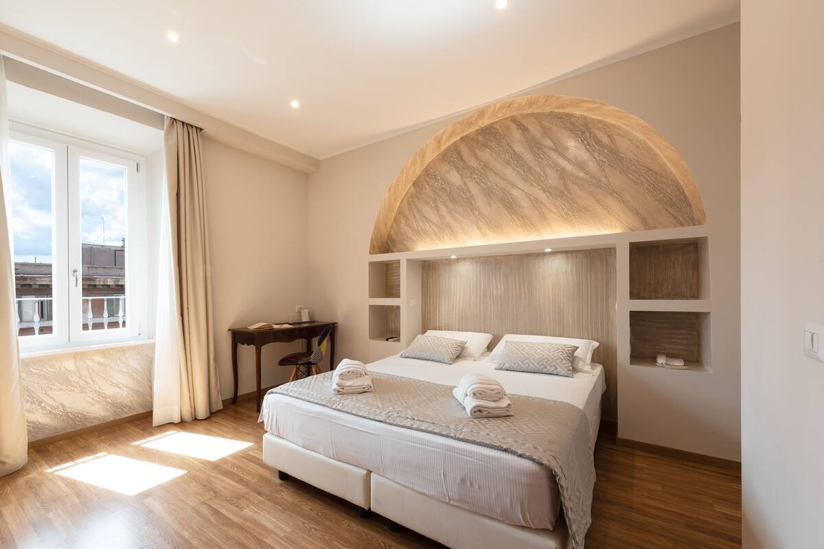 A modern bedroom with a large bed, a curved wall feature, and a desk with a chair.