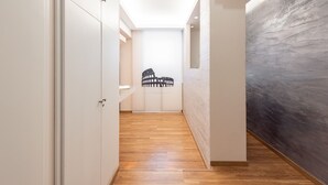 A narrow hallway with wooden flooring, white walls, and a black and white artwork on the wall. - Top Floor Colosseo (Rome)