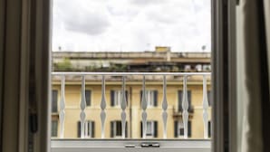 A window with a white balustrade and a view of buildings in the background. - Top Floor Colosseo (Rome)