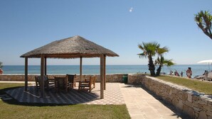 A gazebo with a thatched roof, outdoor seating, and a view of the sea. - Racar Hotel & Resort (Lecce)