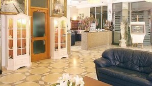 A hotel lobby with a reception desk, a blue leather sofa, a coffee table with a floral arrangement, and a chandelier. - Racar Hotel & Resort (Lecce)