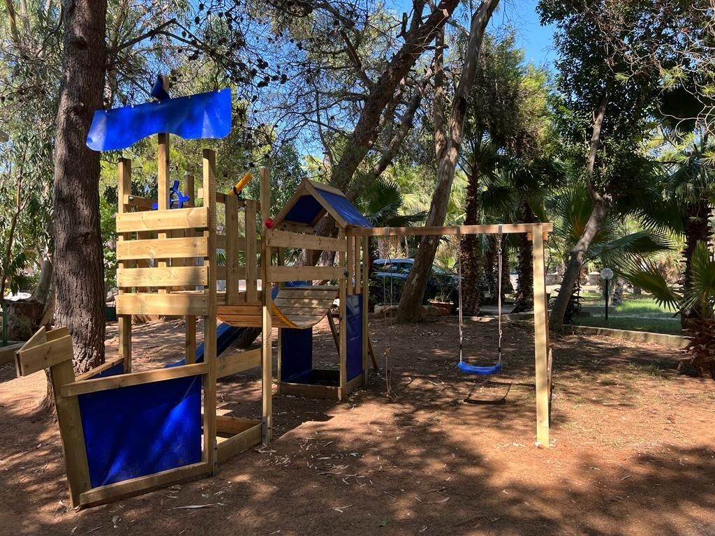 A wooden playground structure with a slide, climbing area, and swing set.