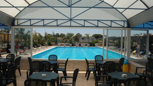 A covered pool area with lounge chairs and tables, a clear view of the pool, and a glass ceiling structure. - Racar Hotel & Resort (Lecce)