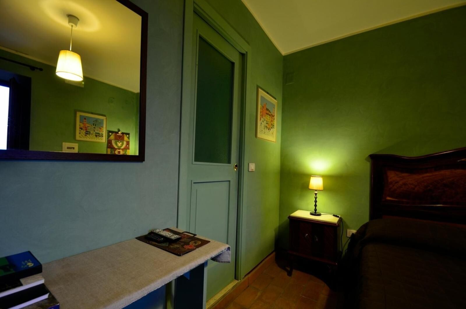 Een kamer met een bed, een nachtkastje met een lamp, een spiegel en een deur.
