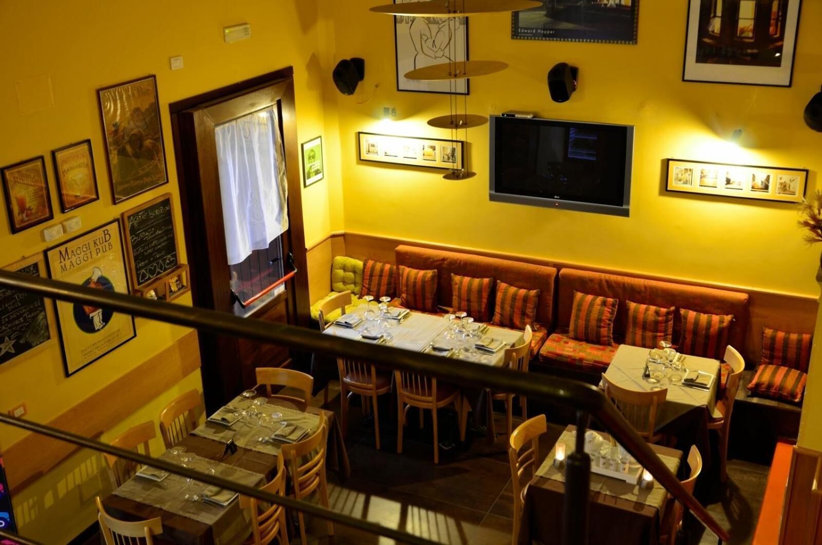A restaurant with a long dining table, multiple booths, and a TV mounted on the wall.