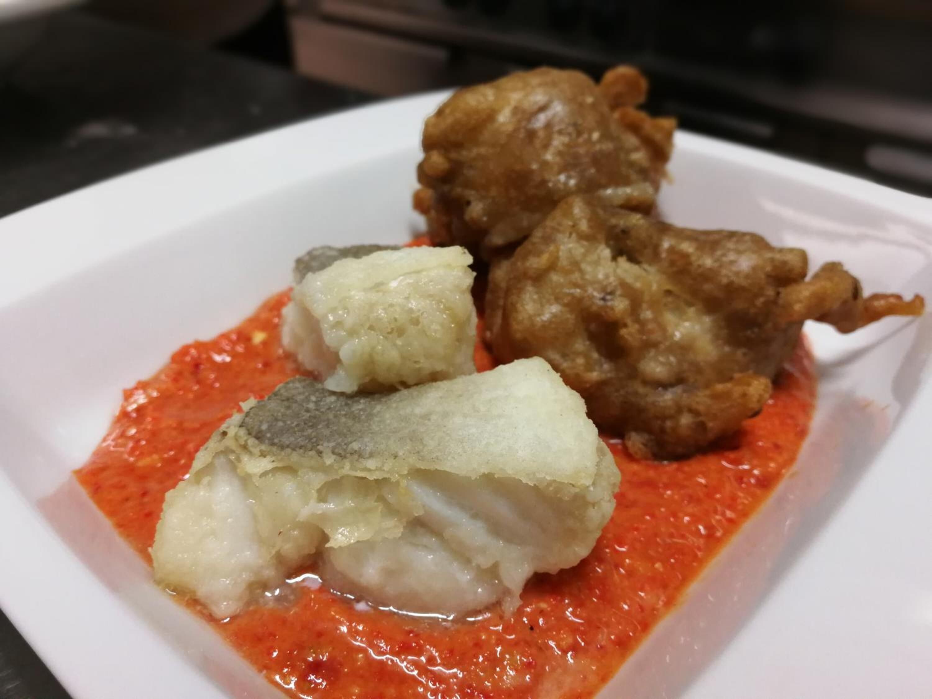A white plate with a fish dish and a red sauce.