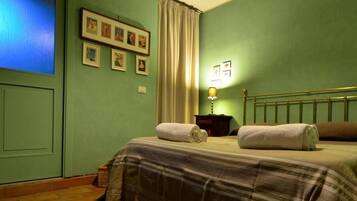 Un dormitorio con cama, mesita de noche, lámpara, ventana con cortinas e imágenes enmarcadas en la pared.