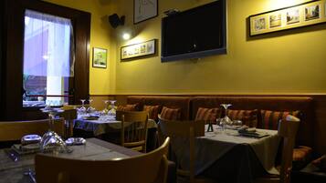 Un restaurante con mesas dispuestas para comer, un televisor montado en la pared y fotografías enmarcadas.