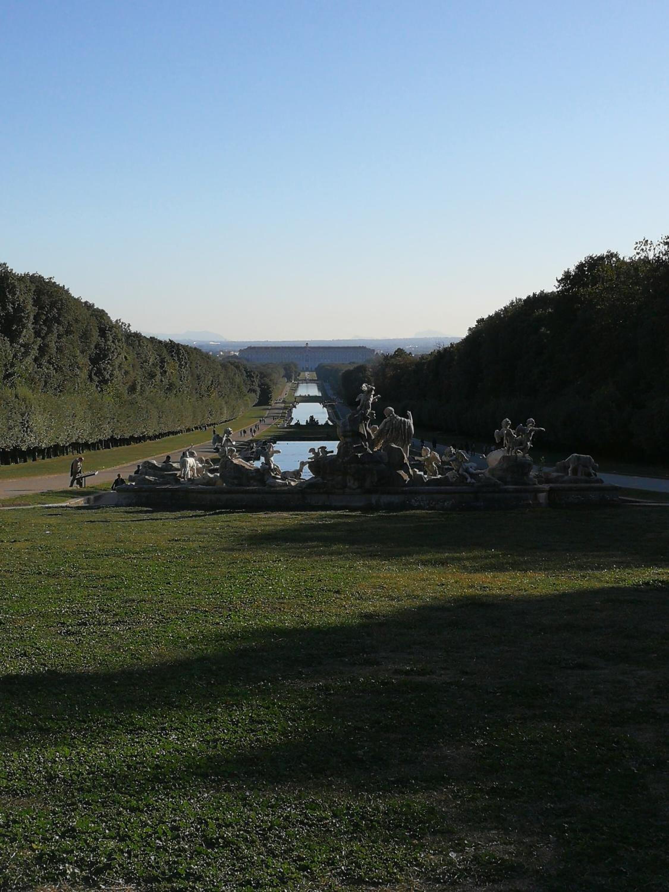 Un parque con una estatua de un jinete a caballo, una fuente y un edificio a lo lejos.