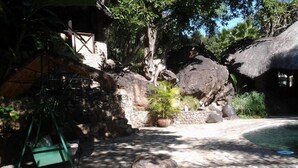 A stone pathway leading to a pool area with a thatched-roof structure and potted plants. - Sethule Lodge (Bulawayo)