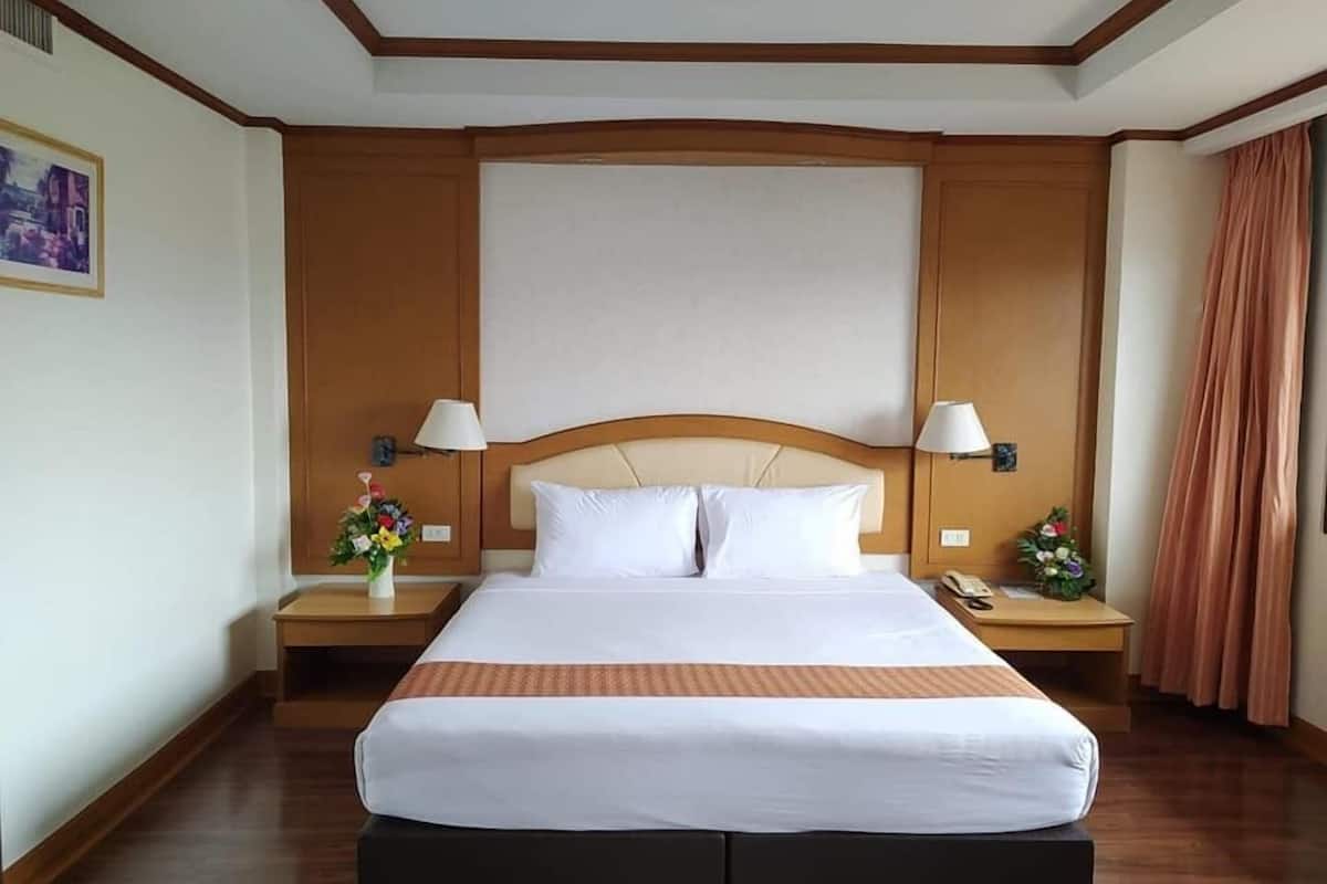 A hotel room with a large bed, wooden headboard, two bedside tables with lamps, and a nightstand with a phone.