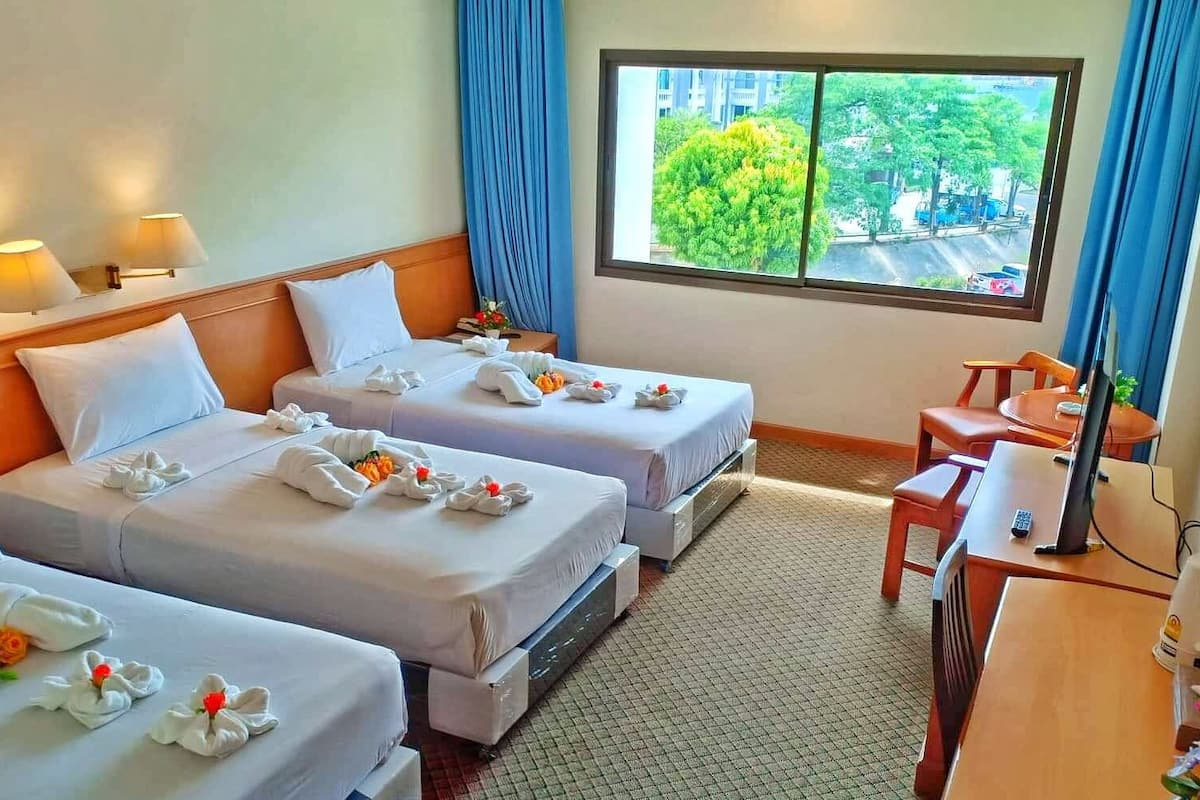 A hotel room with two beds, a desk, a chair, a TV, and a window with a view of trees and buildings.