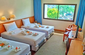 A hotel room with two beds, a desk, a chair, a TV, and a window with a view of trees and buildings. - Sing Golden Place Hotel (Hat Yai)
