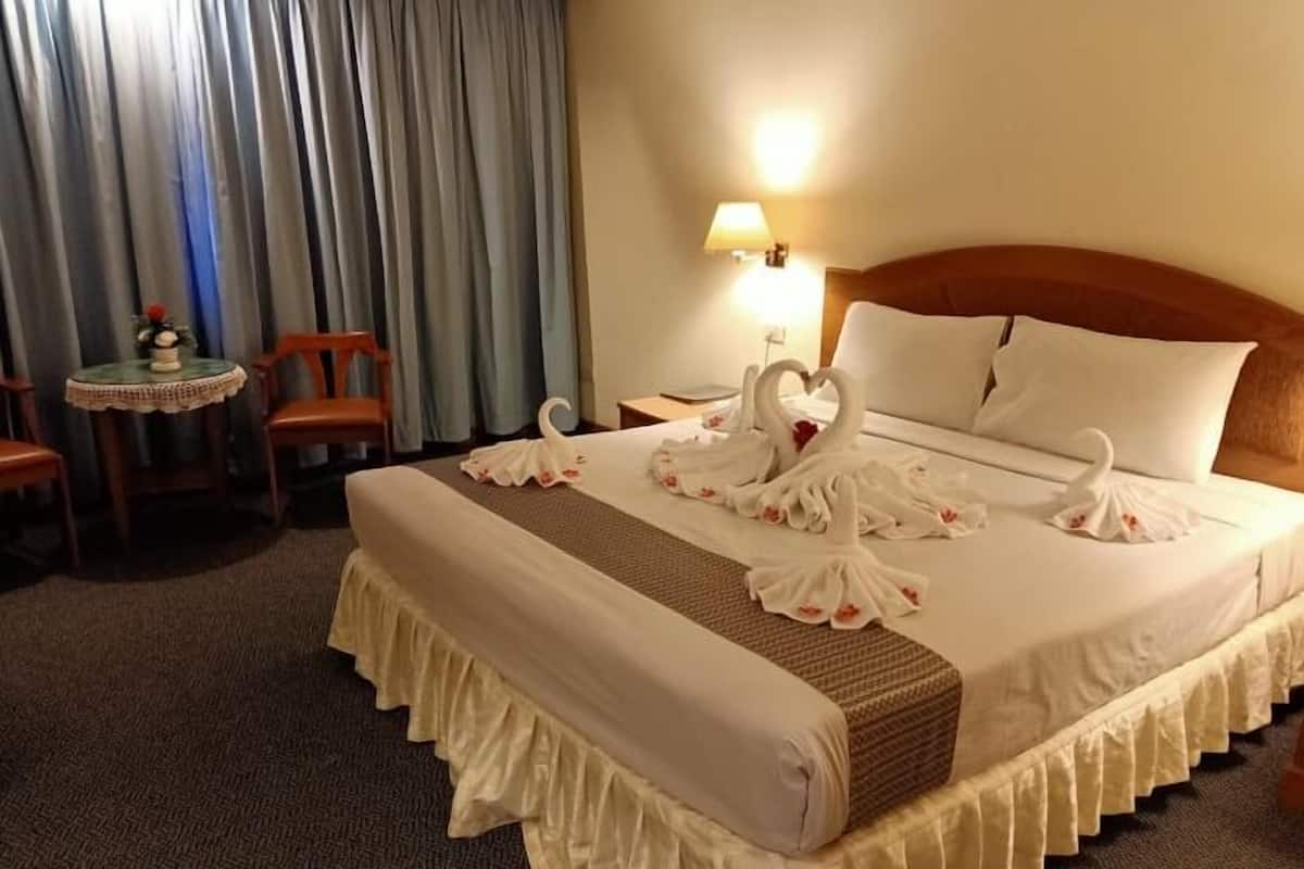 A hotel room with a neatly made bed, a bedside lamp, a small table with a vase, and a chair.
