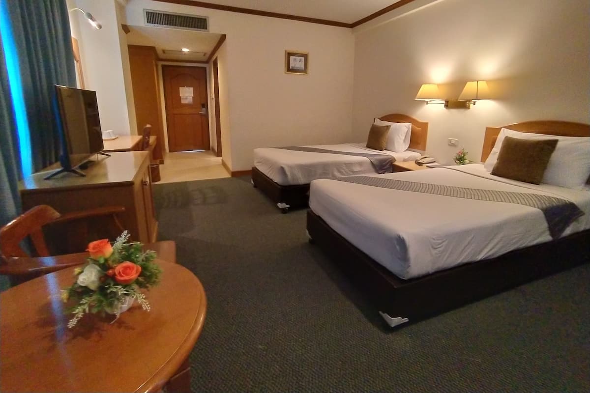 A hotel room with two beds, a desk, a chair, and a small table with a flower arrangement.