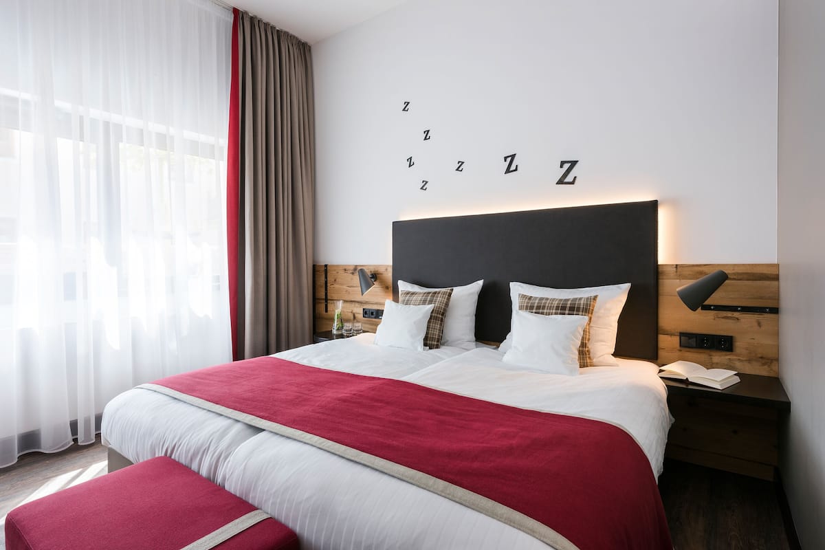 A hotel room with a large bed, a wooden headboard, a bedside table with a lamp, and a wall with letters spelling "Zzz".