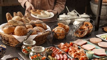 A buffet with various breads, pretzels, and meats.